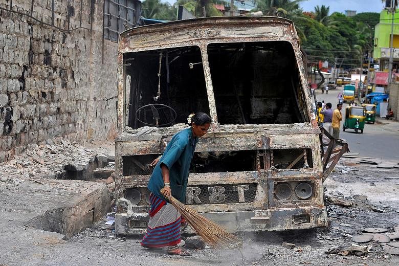 A municipal worker on Wednesday sweeping around the charred remains of a lorry that was set ablaze during violent protests in Bengaluru this week over a water dispute. Employers say the violence did no major damage to the technology hub's appeal.