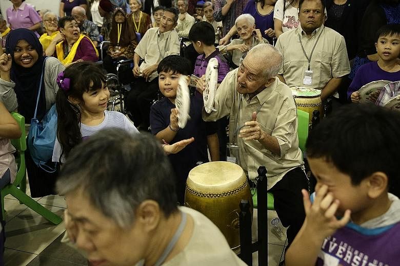 Mr Loh Soh Chye, 77, playing the drum and cymbals with six-year-olds Emily Yuliani Fichera (far left) and Ezra Gabriel Dela Cruz. Mr Loh was one of 38 residents from Apex Harmony Lodge who participated in an intergenerational exchange with 59 childre