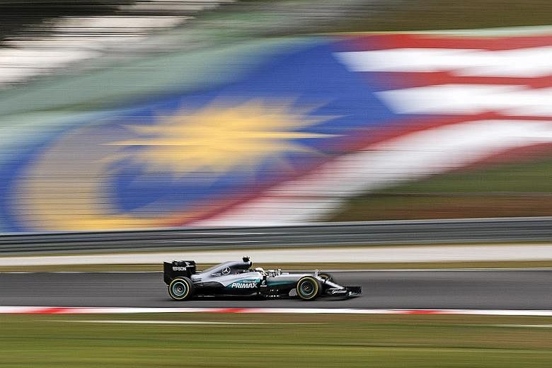 Lewis Hamilton of Mercedes steering his car past a Malaysian flag during the qualifying session for the Malaysian Grand Prix in Sepang yesterday. He starts in pole position for today's race, ahead of team-mate and title rival Nico Rosberg.