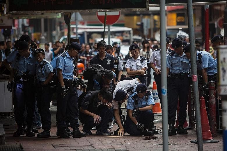 Police officers examining the scene of a knife attack on a man in Hong Kong's Yau Ma Tei district yesterday. Police say they fired shots to stop five or six men from attacking another man. Two assailants and the knife attack victim were wounded.