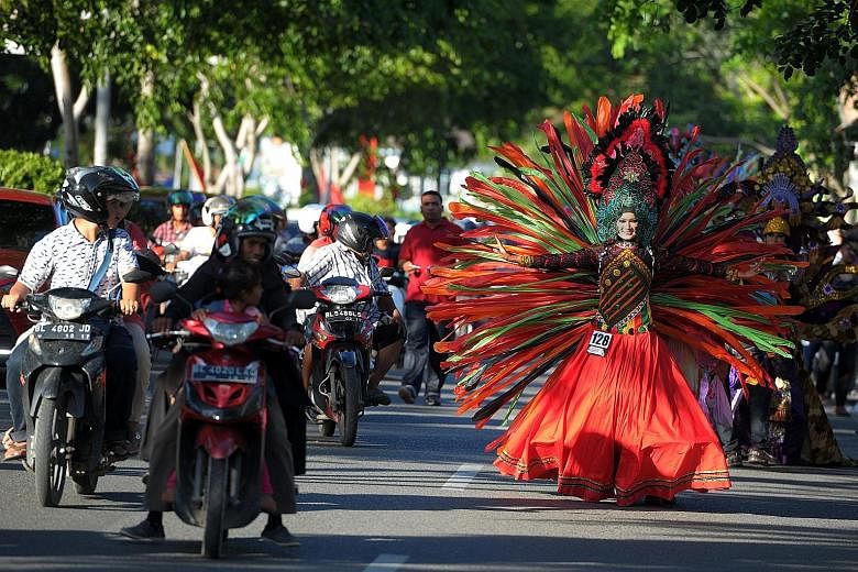 An Acehnese model (left) dressed in an explosion of colours brings traffic to a stop at a fashion show along the streets during Aceh Fashion Week in Banda Aceh, while another model (above) presents a creation by a local designer. Most of the designs 