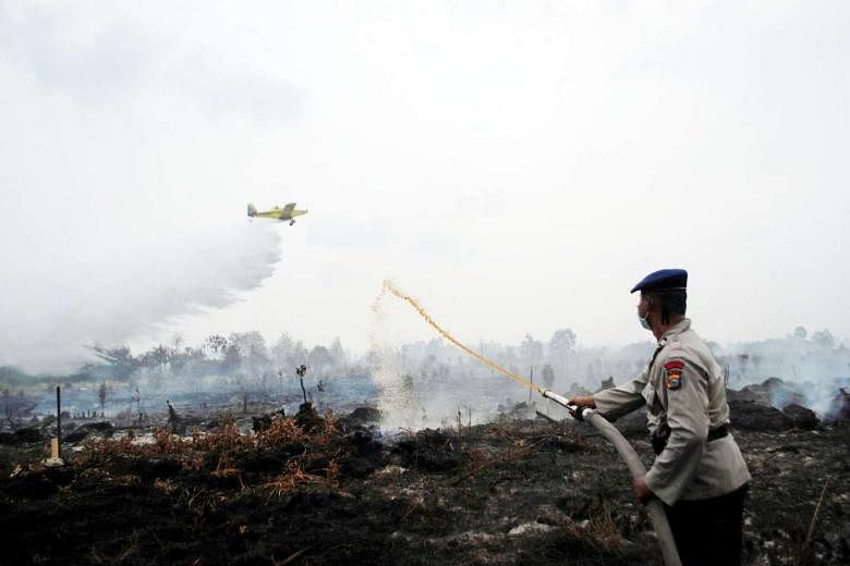 A water bomber dropping its payload as a police officer tried to extinguish a peat fire in Sumatra in August. Some 70 billion tonnes of carbon have built up in peatlands in Indonesia over millennia. 