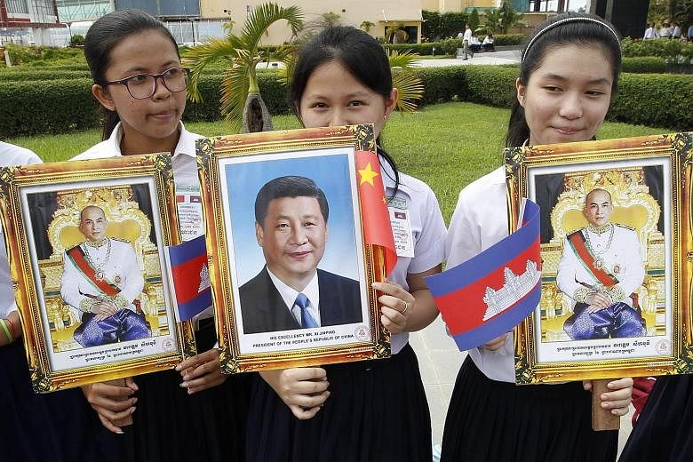 Students with portraits of Cambodian King Norodom Sihamoni and Mr Xi at Phnom Penh's international airport yesterday. At least 28 deals were set to be inked when Mr Xi met Cambodian PM Hun Sen.