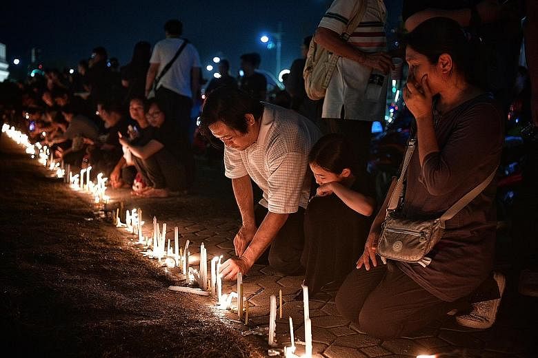 Mourners praying as they light candles during a vigil for Thai King Bhumibol Adulyadej outside the walls of the Wat Phra Kaew, or the Temple of the Emerald Buddha, which is located within the grounds of the Grand Palace, yesterday.