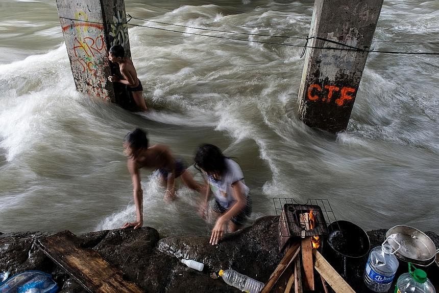 Children playing at a swollen creek in Manila yesterday. In the Philippines, Typhoon Sarika unleashed heavy rain and strong winds on northern rice-growing regions, but there were no confirmed casualties, said officials. Houses partially submerged in 