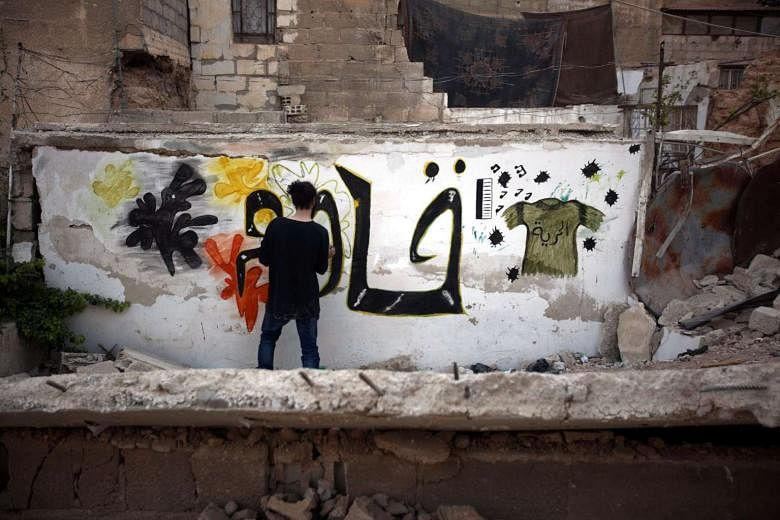 Syrian graffiti artist Noor creating graffiti that reads "Fight, Resist" on a destroyed wall in a rebel-held neighbourhood on the outskirts of Damascus in Syria on Sunday. More than 250,000 people are under government siege in the city of Aleppo, once Syr