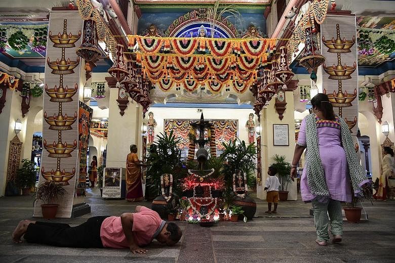 A devotee prays in front of the temple's main prayer hall. Many of the early devotees were Hindus from South India who came to Singapore to work as coolies, craftsmen or merchants. Top: The Sri Mariamman Temple, an enduring icon in Chinatown, has bee