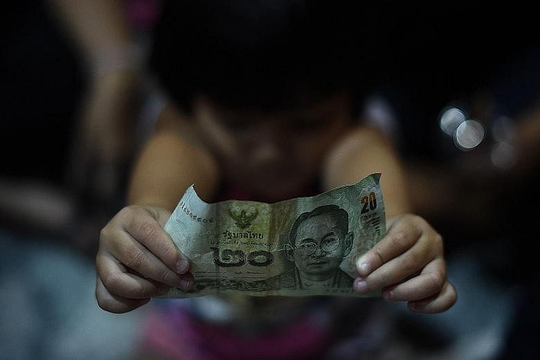 A Thai girl holding up a banknote with the image of Thai King Bhumibol Adulyadej as people paid their respects to the late monarch in a park beneath Bhumibol Bridge in Bangkok last Wednesday.