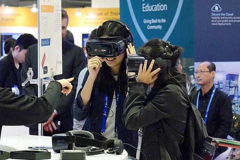 Visitors trying out virtual reality goggles at the FireEye booth (left) and a Cisco exhibition worker (above) during the Singapore International Cyber Week at Suntec Convention and Exhibition Centre earlier this month. Studies have found that cyber a