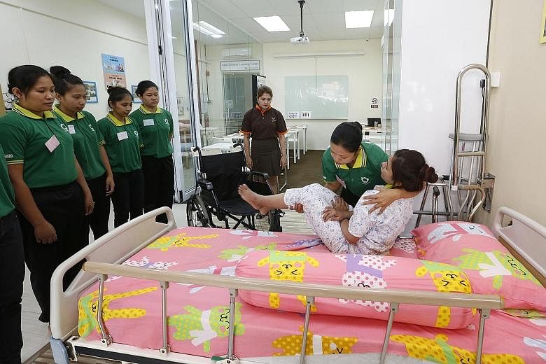 Ms Dewi Narita (left), 37, learning how to help a patient out of bed into a wheelchair and vice versa, at employment agency Homekeeper's training centre in Upper Weld Road, Little India on Saturday. The Ministry of Manpower scheme has matched over 30