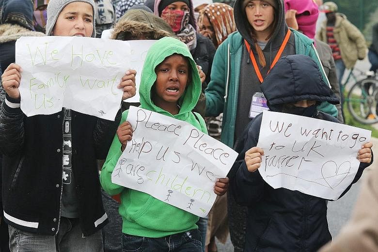 Children holding posters pleading for help at the Calais migrant camp on Wednesday. The posters read: "Please, please help us, we are children" and "We want to go to UK faster".