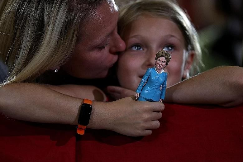 A young Clinton supporter (above) with a doll of the Democratic presidential nominee at a campaign rally in Ohio earlier this month, while a Trump supporter (below) waits for the Republican presidential candidate to speak at a campaign rally in the s
