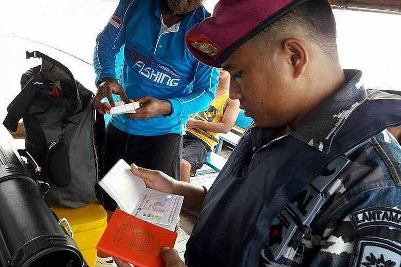 A member of the Indonesian Navy inspecting the passports of the Singaporean anglers caught sailing in an unlicensed boat off Bintan.