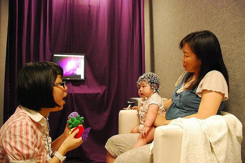 A baby wears sensors that track brain activity in a study that tested the difference in how babies reacted to "standard" and "oddball" sound stimuli. The research, done by Dr Anne Rifkin-Graboi and Dr Cai Shirong (left), found that those babies whose