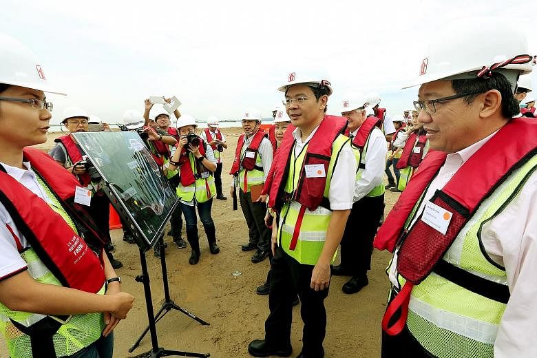 Right: National Development Minister Lawrence Wong being briefed by HDB engineer Chia Siok Teng during his site visit to Pulau Tekong yesterday. Beside him were HDB chief executive Cheong Koon Hean (partially blocked) and HDB group director (building