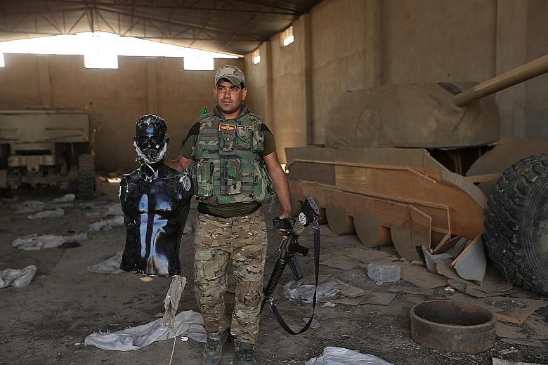 A soldier north of the Iraqi city of Mosul holds a mannequin as he stands beside a wooden tank that was used by militants from the Islamic State in Iraq and Syria to confuse air forces.