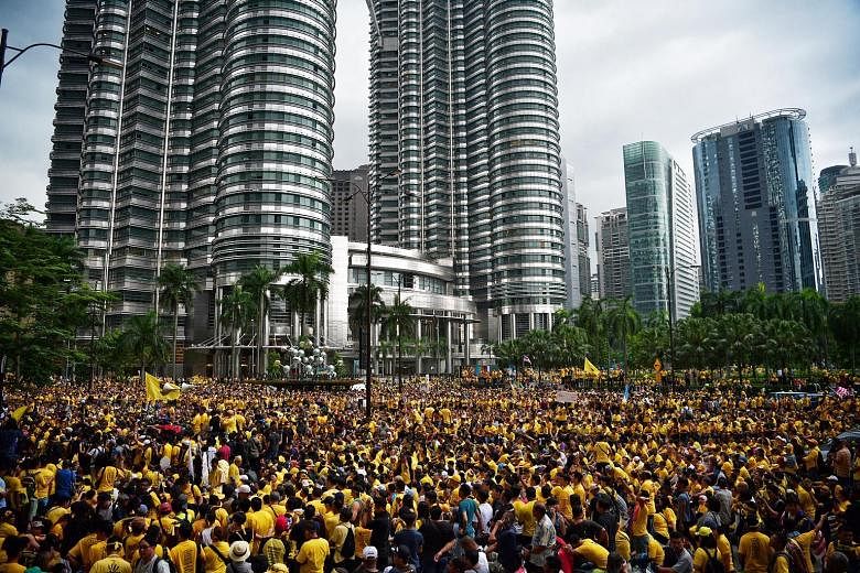 Dr Mahathir waves the Bersih flag (above) as he and former DPM Muhyiddin (behind him) greet the crowd at the Bersih 5 rally in the Malaysian capital Kuala Lumpur. Bersih supporters (right) turned the area around Petronas Twin Towers into a sea of yel
