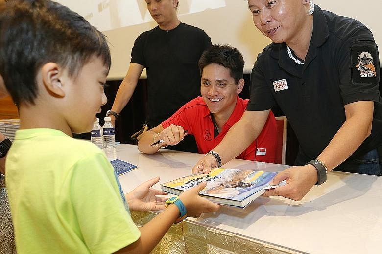 Six-year-old Jayden Kok getting his copy of a book on Olympic champion Joseph Schooling back after the star signed it at the Singapore Press Holdings News Centre yesterday. The 21-year-old swim star autographed copies of two books published by Strait