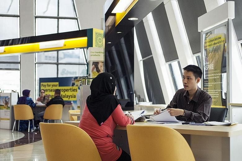 An employee serving a customer at a Maybank branch in Kuala Lumpur. The bank yesterday reported a 5.4 per cent fall in third-quarter profit to RM1.8 billion (S$581 million).