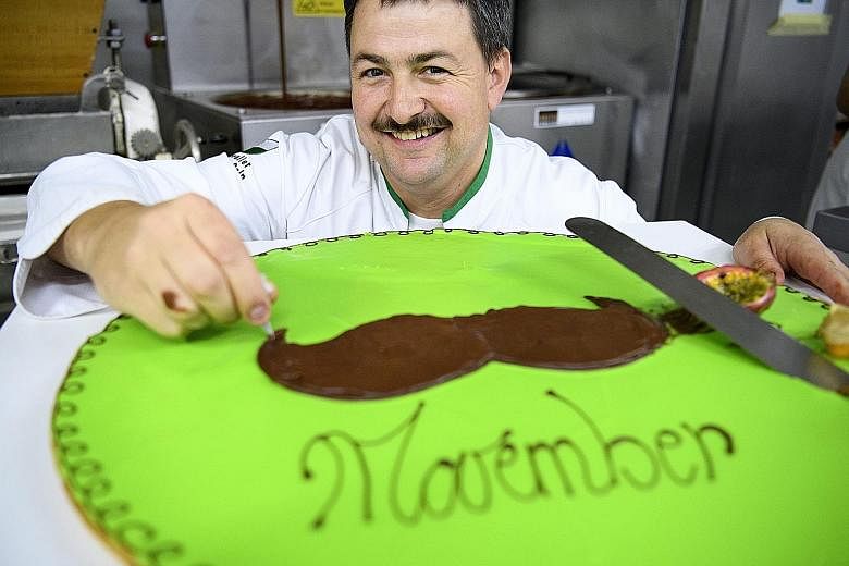 Baker Pascal Clement decorating a chocolate pastry with a moustache to raise funds for the Movember Foundation in Daillens, Switzerland, yesterday. The chocolate pastry which measures 55cm in diameter, weighs between 7kg and 8kg. It will be sold to r