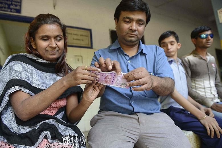 Visually impaired teacher Dilipbhai Chauhan (second from left) on Monday teaching a girl how to identify a new 2,000-rupee note at the Blind People's Association in Ahmedabad. New 500- and 2,000-rupee notes carry improved identification markings for 
