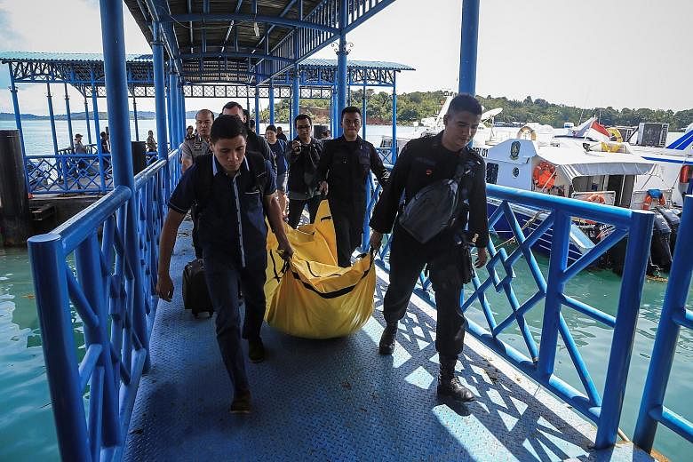 Police officers with a body bag containing debris and belongings recovered from the crash site. The body found near the crash site will be taken to Batam for identification. Investigations indicate that there were initially 16 people on board, but th
