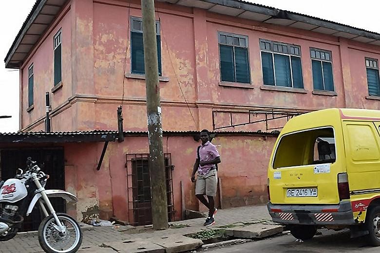 The fake US embassy in the Ghanaian capital Accra is a dilapidated, orange-walled building with rain damage, surrounded by a cracked and buckled sidewalk.