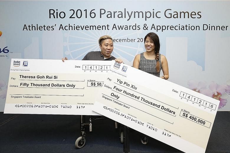 Yip Pin Xiu (far right) smiles as fellow Paralympic medallist Theresa Goh tries to hold up both their cheques at the Athletes' Achievement Awards Reception at Suntec Convention and Exhibition Centre.