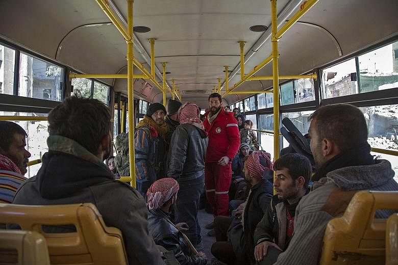 A staff member of the Syrian Red Crescent standing in a bus with rebel fighters and their families during the evacuation operation from Aleppo yesterday. The first convoy, which includes 13 ambulances and 20 buses, is making its way to rural parts of