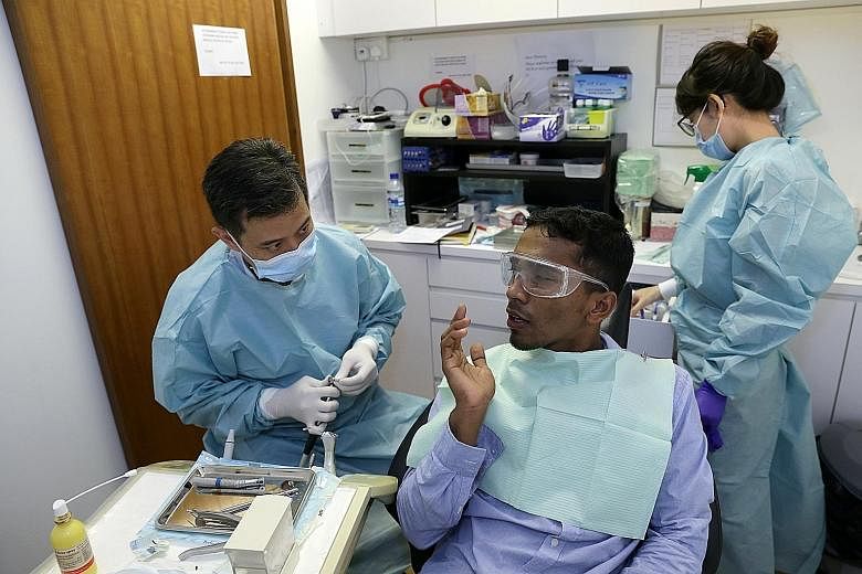 Bangladeshi construction worker Ahammad Rubal getting a tooth filling done by Dr Winston How, who is assited by dental student Sophia Choo (right). Foreign workers waiting to see a doctor at HealthServe's Geylang clinic. The workers pay $5 a visit.