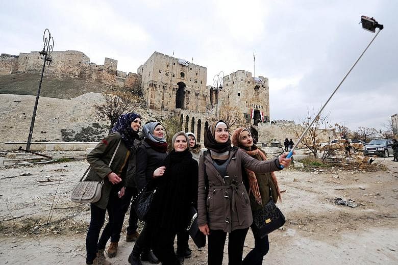 Women posing for photographs outside Aleppo's historic citadel (above) and at the entrance of the Carlton Citadel Hotel (below), both in a government-controlled area of the city, last Saturday. With the battle for Aleppo reaching its final stages, vi
