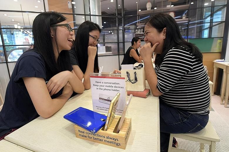 Some Toast Box customers receive a $5 voucher if they leave their mobile phones in a phone holder on the table while they eat or drink. The initiative is aimed at encouraging people to talk to each other more. From left: Ms Alene Ku with her sister B