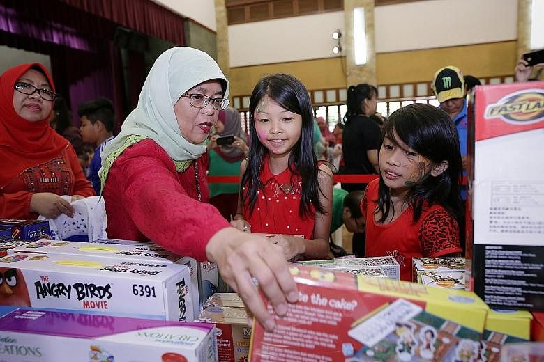Madam Halimah helping Crystal Hoe, 10 (right), and Lim Yungfang, 11, choose their presents at yesterday's Toys Carnival @ Marsiling.