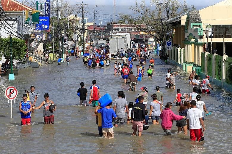 Residents making their way along a street flooded by heavy rain brought by Typhoon Nock-Ten, which cut through Naboa town in the Bicol region of central Philippines yesterday. More than 400,000 people had to be evacuated from their homes due to the t