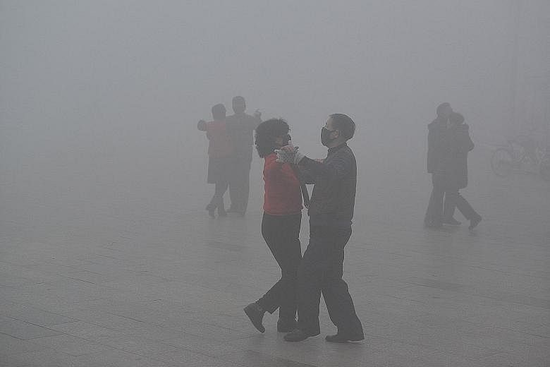 A police officer dons a face mask on a road in foggy Beijing yesterday. Drivers were advised to slow down to safe speeds, and airports, highways and ports were told to take the necessary safety measures. People wearing masks dance at a square despite