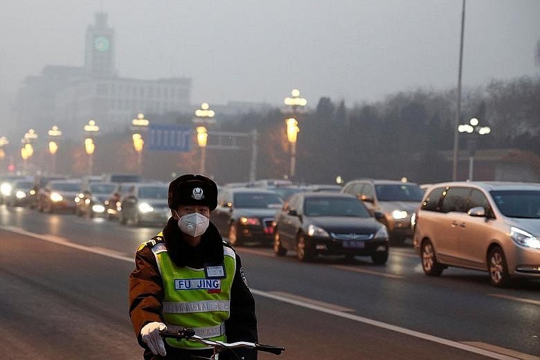 A police officer dons a face mask on a road in foggy Beijing yesterday. Drivers were advised to slow down to safe speeds, and airports, highways and ports were told to take the necessary safety measures. People wearing masks dance at a square despite