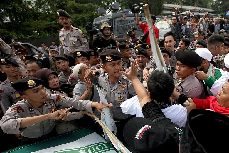 Police officers trying to calm down protesters who gathered to demonstrate against Jakarta governor Ahok (above) outside the trial venue yesterday.