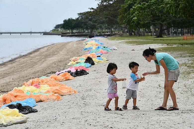Oil floating on water near mangroves at Pulau Ubin yesterday. Cleanup operations were carried out on a 100m stretch of Noordin beach. A mother with her two children picking up seashells yesterday on Changi beach, which was lined with bags filled with
