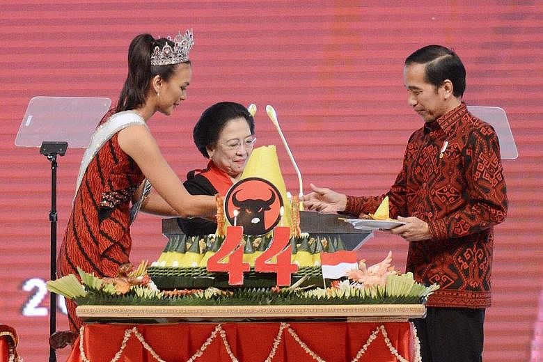 Ms Megawati (centre) serving President Joko rice from the top of a tumpeng - a traditional Javanese celebratory meal of yellow rice and other dishes. She is assisted by Ms Indonesia Kezia Warouw.
