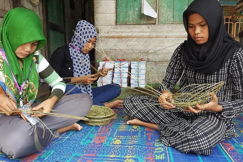 Women from the village using stalks from the oil palm leaves to weave baskets. As part of the "no-burn" method, farmers are taught to turn vegetative debris and wood waste into fertiliser for their crops. Thicker pieces of wood are sold to furniture-