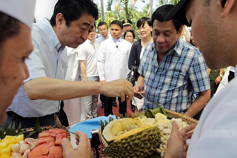 President Rodrigo Duterte giving Japan's Prime Minister Shinzo Abe (left) a tasting of durian, a key export of Davao, yesterday. Mr Abe has sought to woo the Philippines with a US$9 billion (S$12.8 billion) aid package, and has offered to help Mr Dut