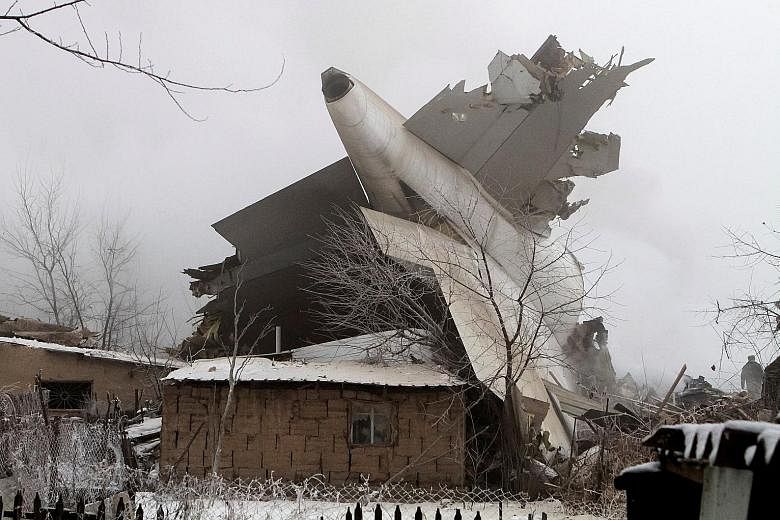 A big section of the aircraft (above) sticks out of a home at the crash site of a Turkish cargo jet near Kyrgyzstan's Manas airport, outside the capital Bishkek, yesterday. Rescue officials were seen recovering bodies at Dacha-Suu (below). At least 3