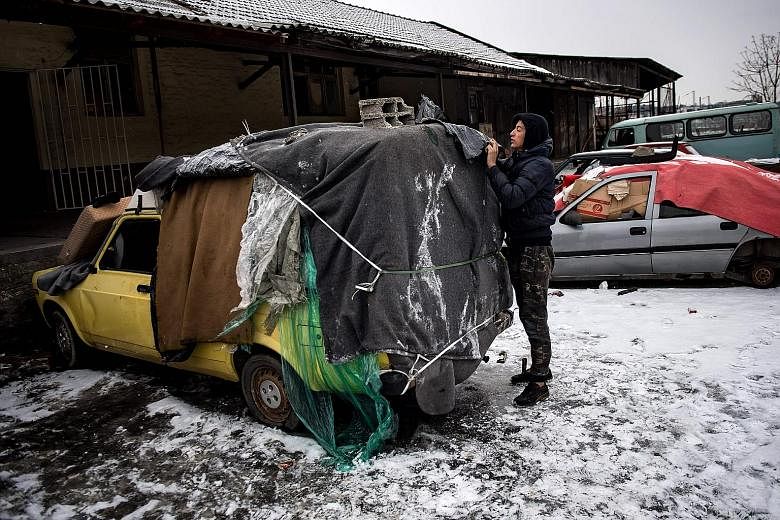 A migrant covering an abandoned car he uses as a makeshift shelter near Belgrade's main railway station yesterday, as temperatures plummeted drastically below 0 deg C. According to the latest figures, around 7,000 migrants are stranded in Serbia.