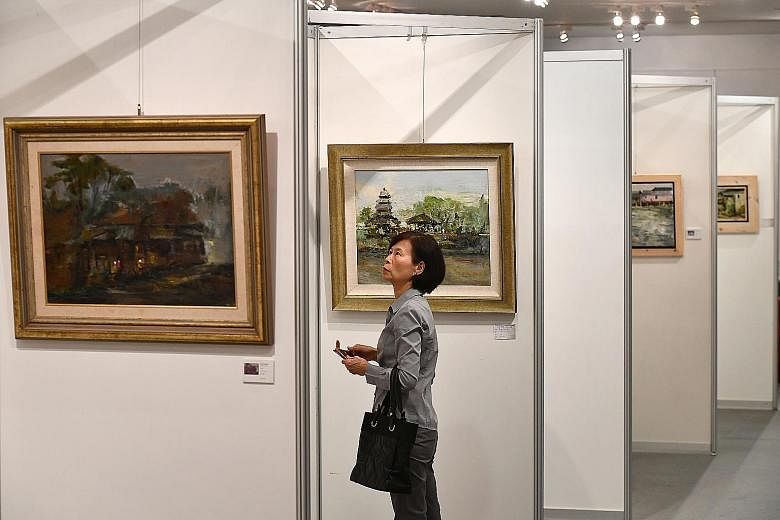 Madam Sharon Chow, a housewife in her 40s, looking at oil paintings at an exhibition by artist and retired art teacher Tan Choo Kai yesterday evening. Tapestry Of Nature, Mr Tan's latest solo exhibition, features 99 oil paintings and was launched yes