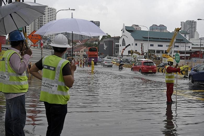 Workers from a nearby construction site directing traffic away from rising flood waters. Upper Thomson Road was hit by a second flash flood in as many months yesterday, with photos on social media showing vehicles with up to half their tyres in water
