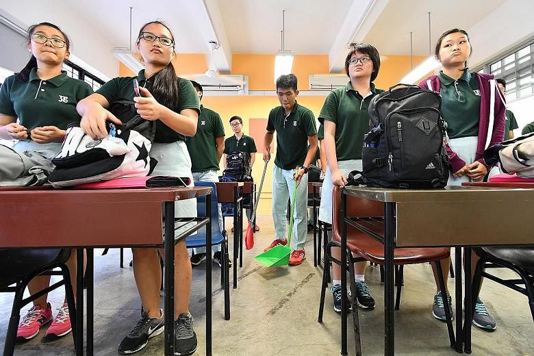 TPJC student Jaydon Chong Wei Ler (centre) sweeping the floor after a lesson. First-year students at the junior college assist the cleaners, even with cleaning the toilets, as part of Project Kirei, a student-driven initiative.