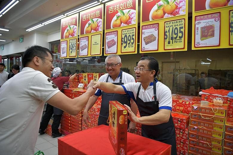 FairPrice chairman Mr Chin (centre) and chief executive Mr Seah (right) manning the mandarin orange booth at a Toa Payoh outlet yesterday. Mr Seah said that attachments at the stores help office staff to understand the challenges faced by front-line 
