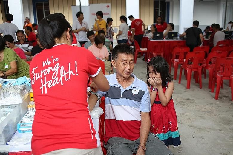 Chia Yi Leng, eight, trying to put on a brave front while her father, Mr Chia Kwong Weng, 56, prepared to have his blood drawn for a test yesterday. He was among those given free health screenings under a new One and Health Programme that saw some 30