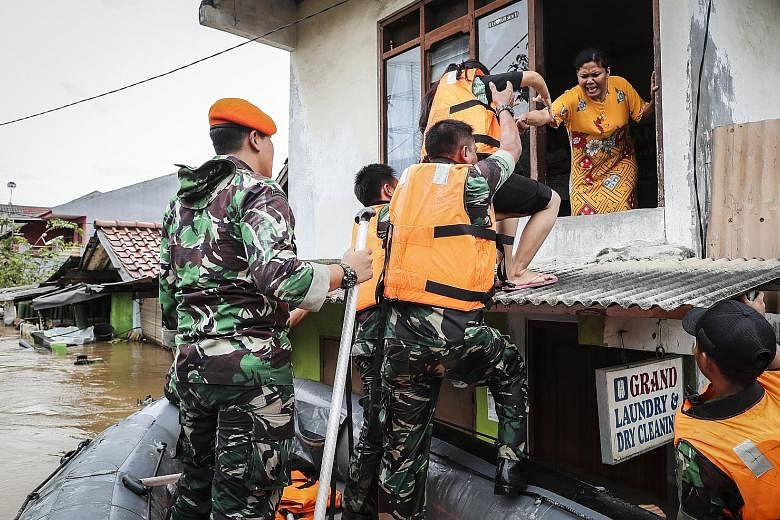 Above: Residents in a flood-hit neighbourhood of Jakarta being helped into a rubber boat yesterday. Left: Indonesian air force soldiers assisting stranded residents as torrential rain triggered widespread flooding.