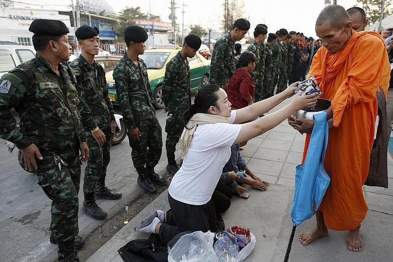 Monks from the controversial temple collecting morning alms outside the compound as soldiers stand guard.